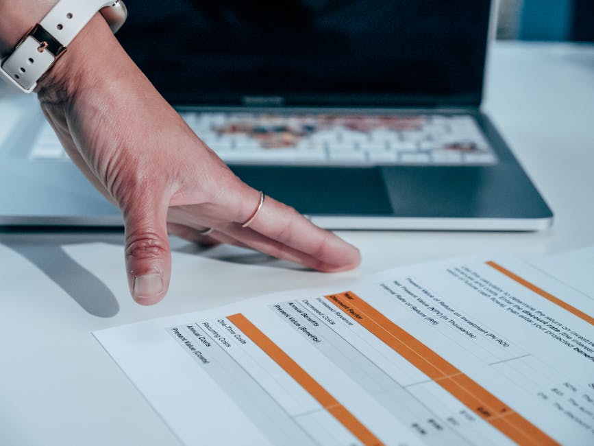Close-up of a hand reviewing a financial report on a laptop, indicating focus on business analysis.